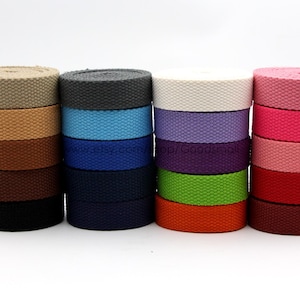 May include: Assortment of 10 colors of cotton webbing, each color stacked in a pile. The colors are beige, gray, white, lavender, purple, pink, red, maroon, green, and orange.