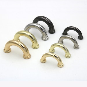 May include: A set of six metal D-rings in various sizes and finishes, including gold, silver, and black. The rings are all in the shape of a half-circle and have a smooth, polished finish.