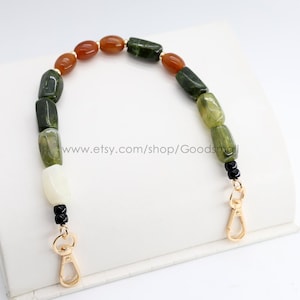 May include: A beaded handbag strap featuring a variety of colorful gemstones. The strap includes green, orange, and white stones, with gold-colored clasps. The text "www.etsy.com/shop/Goodsmal" is visible.