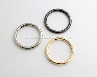 May include: Three circular metal spring rings in silver, gunmetal, and gold tones. Each ring features a small hinge mechanism for opening and closing. The text www.etsy.com/shop/Goodsmall is printed in the center of the three metal rings.