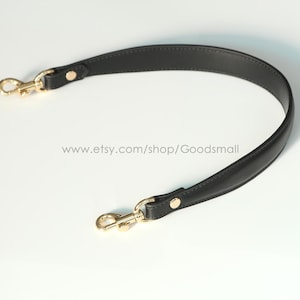 May include: A black leather bag handle with gold-coloured clasps and hardware. The handle is curved and has a smooth texture. The Etsy shop URL www.etsy.com/shop/Goodsmall is visible.