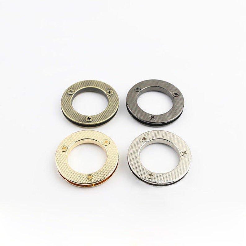 May include: Four metal rings in different finishes: gold, silver, black, and bronze. Each ring has a textured surface and four small screws.