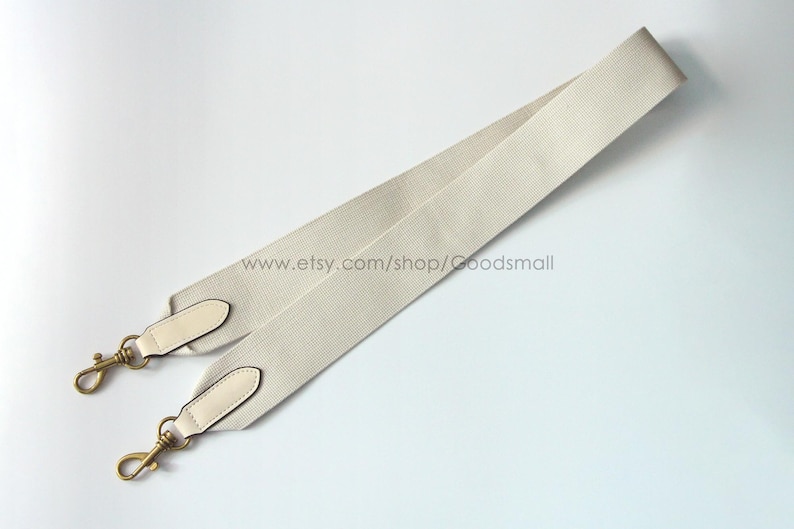 May include: Cream-colored bag strap with gold-tone hardware. The strap is made of a ribbed fabric and features leather accents at the ends. The strap has two gold-tone clasps for attachment. The Etsy shop URL is visible.