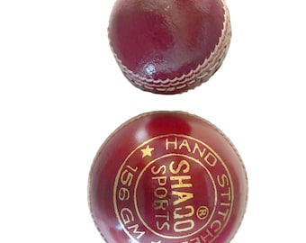 May include: A red leather cricket ball with white stitching. The ball has a gold logo that says "Shaqo Sports" and "Hand Stitched" with a star on either side. The ball weighs 156 grams.