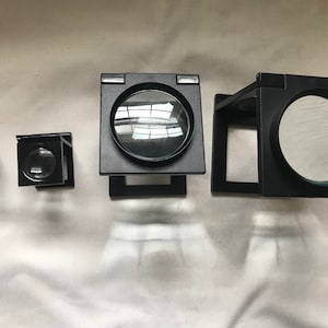 以下が含まれることがあります： 異なるサイズのレンズが付いた黒い虫眼鏡が4つ。虫眼鏡は折り畳み式でスタンドが付いています。
