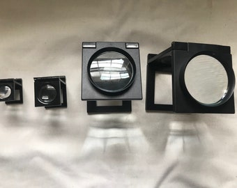 May include: Four black magnifying glasses with different sized lenses. The magnifying glasses are foldable and have a stand.