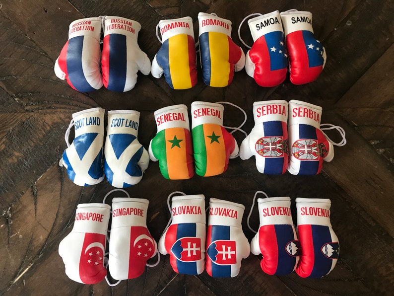 May include: Twelve pairs of miniature boxing gloves, each decorated with a different country's flag. The flags include Russia, Romania, Samoa, Scotland, Senegal, Serbia, Singapore, Slovakia, and Slovenia.