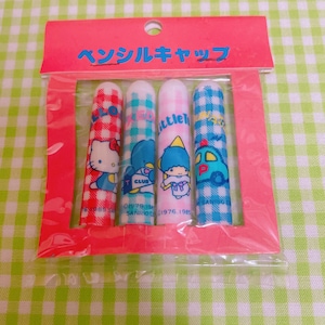 Pode incluir: Um pacote de quatro tampas de lápis com personagens de desenhos animados. As tampas são cilíndricas e decoradas com personagens como Hello Kitty e um carro azul. A embalagem é rosa com texto japonês no topo.