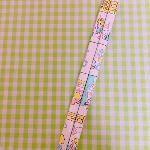 May include: Two pencils with a repeating pattern of cartoon characters and interior scenes. The pencils are light pink with a grid design. The background is a green and white checkered pattern.