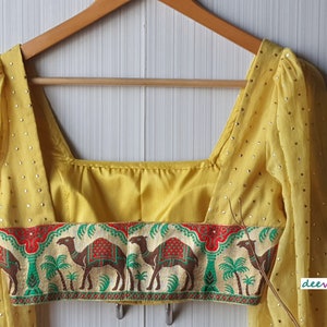 May include: Yellow sleeveless blouse with a square neckline and a camel print trim. The blouse has a sheer fabric with small gold dots.