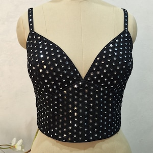 May include: Black crop top with a deep V-neck and thin straps. The top is covered in small, reflective silver sequins. The garment is displayed on a mannequin.