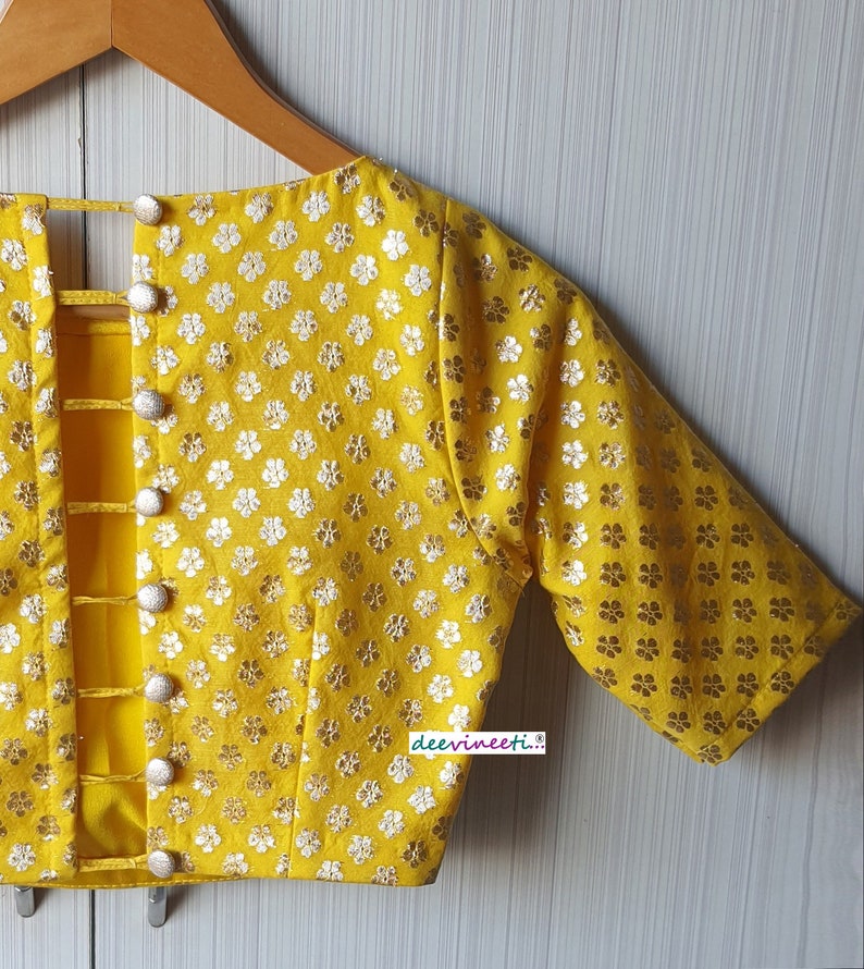 Pu&ograve; includere: Una blusa gialla con motivo floreale e chiusura con bottoni sul retro. La blusa ha maniche corte e scollo rotondo.