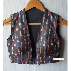 Könnte beinhalten: Eine ärmellose Bluse mit Ikat-Muster in Schwarz und Weiß mit einem tiefen V-Ausschnitt. Die Bluse hat ein schwarzes Futter und ein kleines weißes Etikett mit der Aufschrift "deervineeti..."
