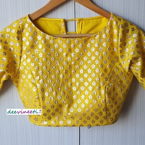 Pu&ograve; includere: Blusa gialla con motivo floreale e maniche corte. La blusa ha una scollatura rotonda e un'apertura a chiave sul retro.