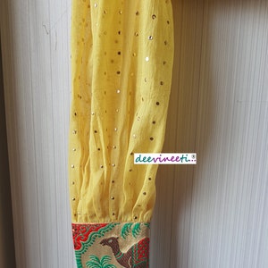 May include: Yellow sheer blouse with gold sequins and a colorful embroidered cuff featuring a camel and palm trees. The cuff has red, green, and gold accents. The text "deevineeti..." is printed on the blouse.