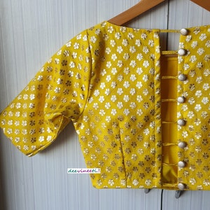 Pu&ograve; includere: Una blusa gialla con motivo floreale e un design posteriore con una serie di chiusure a bottone.