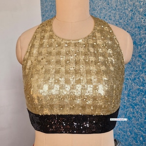 May include: A gold sequined halter top with a black sequined band at the bottom. The top is sleeveless and has a round neckline.