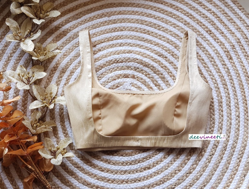 May include: A beige sleeveless blouse with a satin-like finish. The blouse has a scoop neckline and a fitted bodice.
