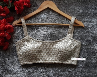 May include: A silver sequined crop top with a scoop neck and thin straps. The top has a subtle pattern of overlapping scales. The text "deevineeti..." is visible in the bottom right corner.