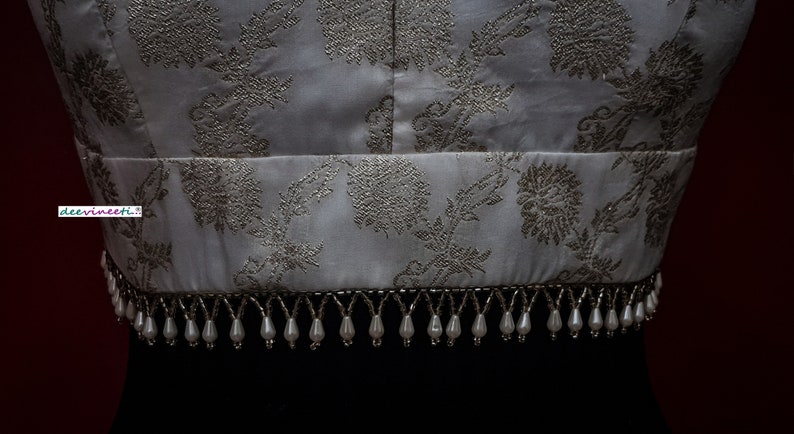 May include: A white top with a silver floral pattern and a beaded trim. The trim is made of white beads with silver accents.
