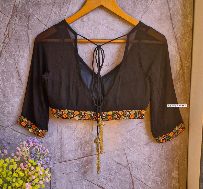 May include: Black sheer blouse with a tie-up back and floral embroidery around the neckline and sleeves. The blouse has a deep V-neckline and is made of a lightweight fabric.