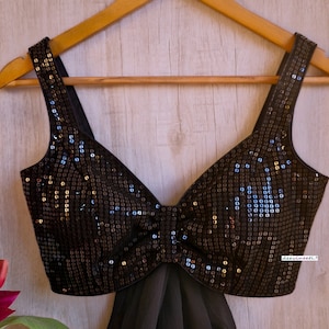 May include: A black sequined crop top with a sweetheart neckline and a bow detail. The top is on a wooden hanger.