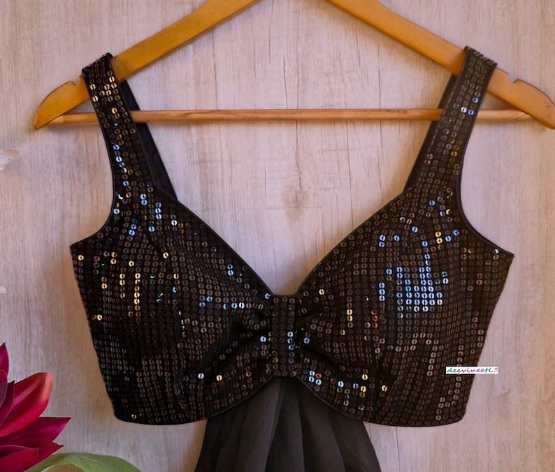 May include: A black sequined crop top with a sweetheart neckline and a bow detail. The top is on a wooden hanger.