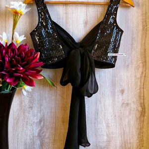 May include: A black sequined crop top with a black chiffon tie at the back. The top has a deep V-neckline and is sleeveless.