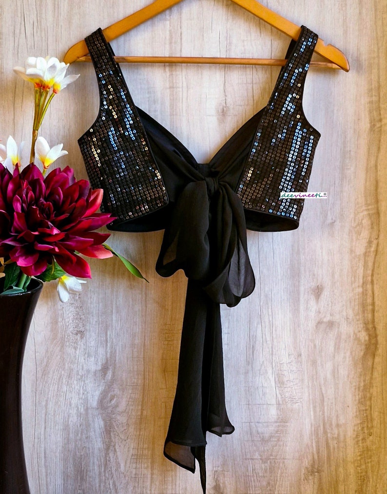 May include: A black sequined crop top with a black chiffon tie at the back. The top has a deep V-neckline and is sleeveless.