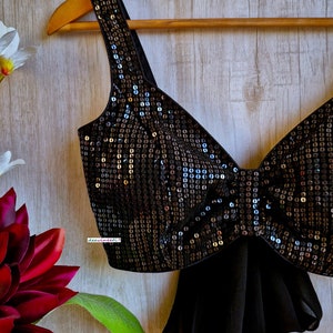 May include: A black sequined crop top with a bow detail and a matching black chiffon scarf. The top is on a wooden hanger.