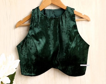 May include: A dark green velvet sleeveless blouse with a round neckline. The blouse is hanging on a wooden hanger against a light wood background.