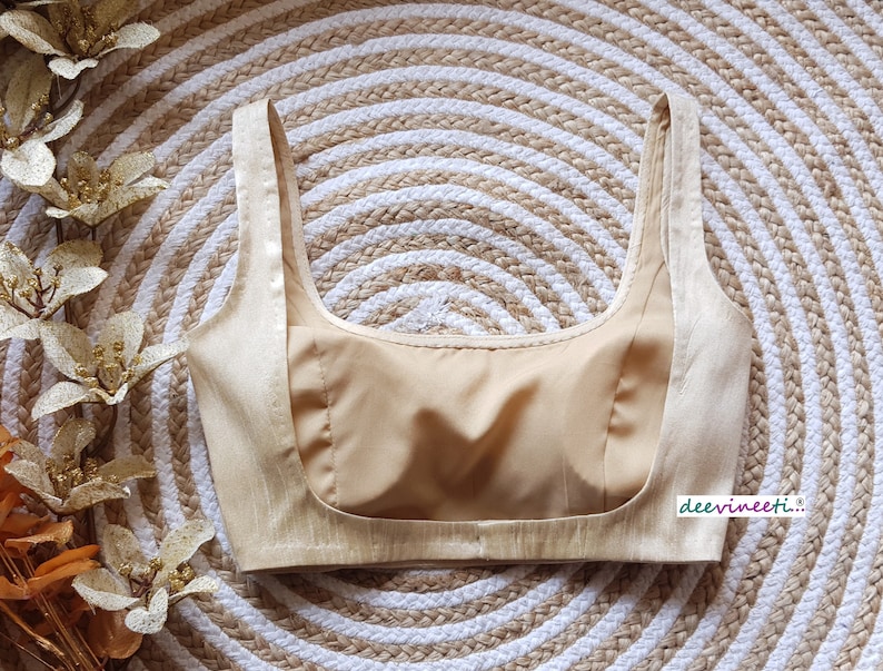 May include: A beige, sleeveless, padded bra with a scoop neck. The bra is made of a silky fabric and has a satin-like finish.