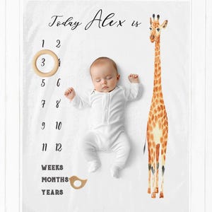 May include: A white baby milestone blanket with a giraffe illustration and the text "Today Alex is". The blanket has numbers 1 through 12, and the words "Weeks", "Months", and "Years".