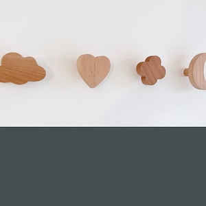 May include: Four wooden wall hooks in the shapes of a cloud, heart, flower, and crescent moon. The hooks are all made of natural wood and have a light brown colour.