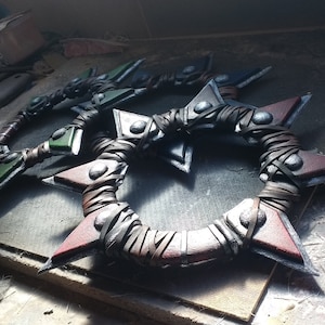May include: Three circular throwing weapons with sharp points. The weapons are wrapped in brown leather and have metal accents. The weapons are painted in shades of green, red, and black.