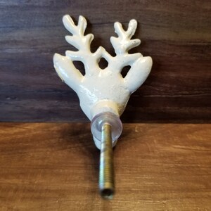 May include: White ceramic reindeer head door knob with a gold screw. The knob has a detailed design of antlers and a face.