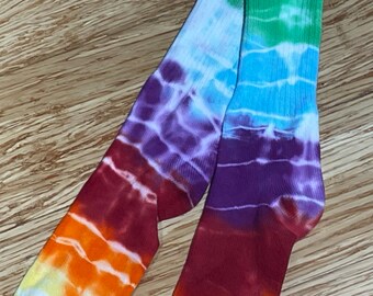 May include: A pair of colorful tie-dye socks with a rainbow pattern. The socks are made of a soft, comfortable material and are perfect for adding a pop of color to any outfit.