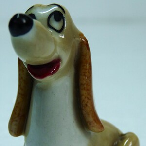 May include: A ceramic figurine of a brown and white dog with floppy ears. The dog has a red mouth and black eyes. The figurine is approximately 10 cm tall.