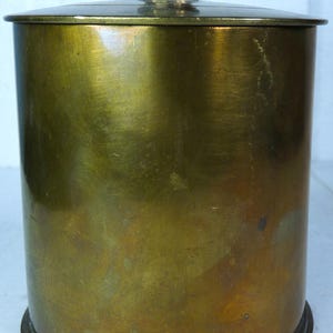 May include: A cylindrical brass container with a lid and a small, decorative knob on top. The container has a polished, aged appearance, with a slightly tarnished surface. The design is simple and classic, suggesting a vintage or antique style.