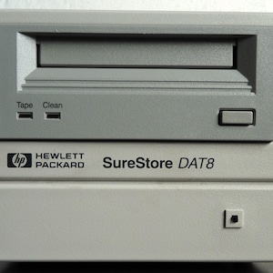 May include: A light gray Hewlett Packard SureStore DAT8 data storage device. The device has a tape slot, a power button, and indicator lights for tape and cleaning. The Hewlett Packard logo is visible on the front.