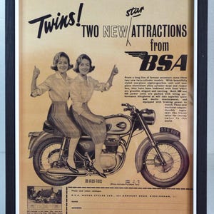 May include: Framed vintage BSA motorcycle advertisement. The sepia-toned print shows two women on a motorcycle, with the text "Twins! TWO NEW ATTRACTIONS from BSA". The ad includes text and a motorcycle illustration.