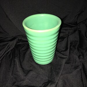 May include: A green ceramic planter with a ribbed design. The planter is empty and has a smooth, glossy finish.
