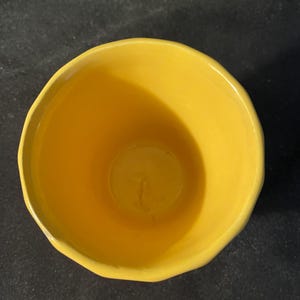 May include: A bright yellow ceramic bowl with a rounded shape and a slightly uneven rim. The interior of the bowl is also yellow, creating a cohesive and vibrant look. The bowl is likely used for serving or holding food items.