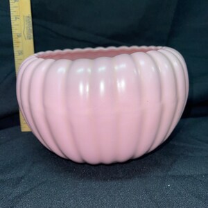 May include: A pink ceramic planter with a ribbed design. The planter is round and has a wide opening.