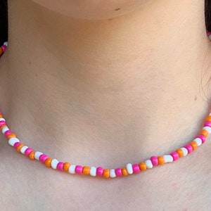 May include: A pink, white, and orange beaded necklace. The necklace is made of small, round beads that are strung together on a thin cord.