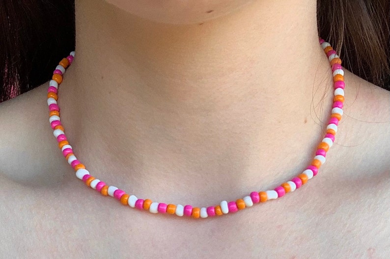 May include: A pink, white, and orange beaded necklace. The necklace is made of small, round beads that are strung together on a thin cord.