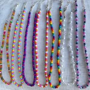 May include: Nine colorful beaded necklaces with various patterns and colors, including pink, blue, green, yellow, and purple.