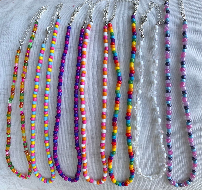 May include: Nine colorful beaded necklaces with various patterns and colors, including pink, blue, green, yellow, and purple.