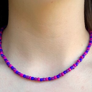 May include: A purple and pink beaded necklace. The beads are small and round, and they are arranged in a repeating pattern of purple and pink.
