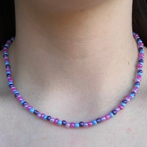 May include: A delicate choker necklace made with small, iridescent beads in shades of pink, purple, and blue.